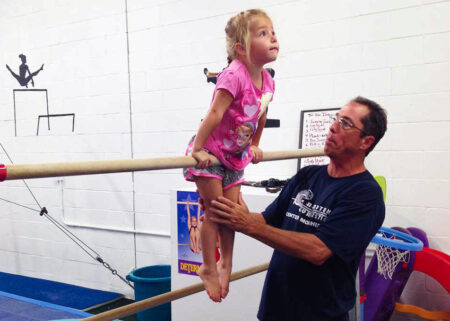 Trainer helping young girl on horizontal bars